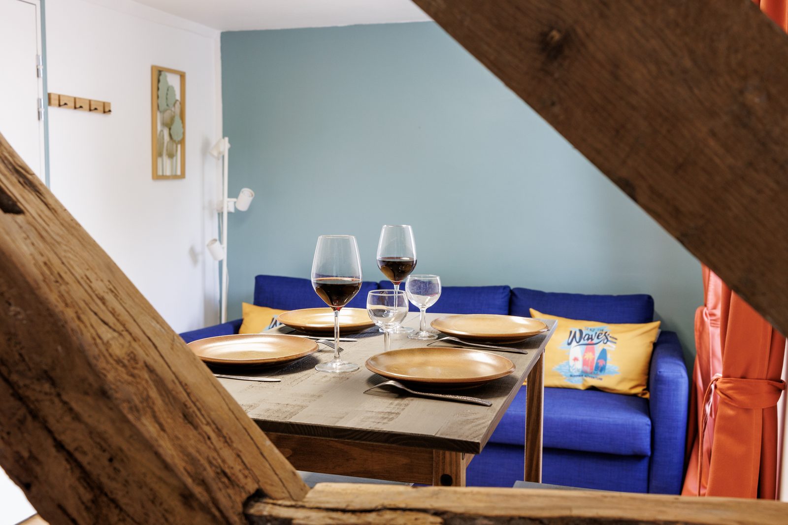 Séjour Le Combi — table repas, canapé bleu et poutres apparentes — KM99