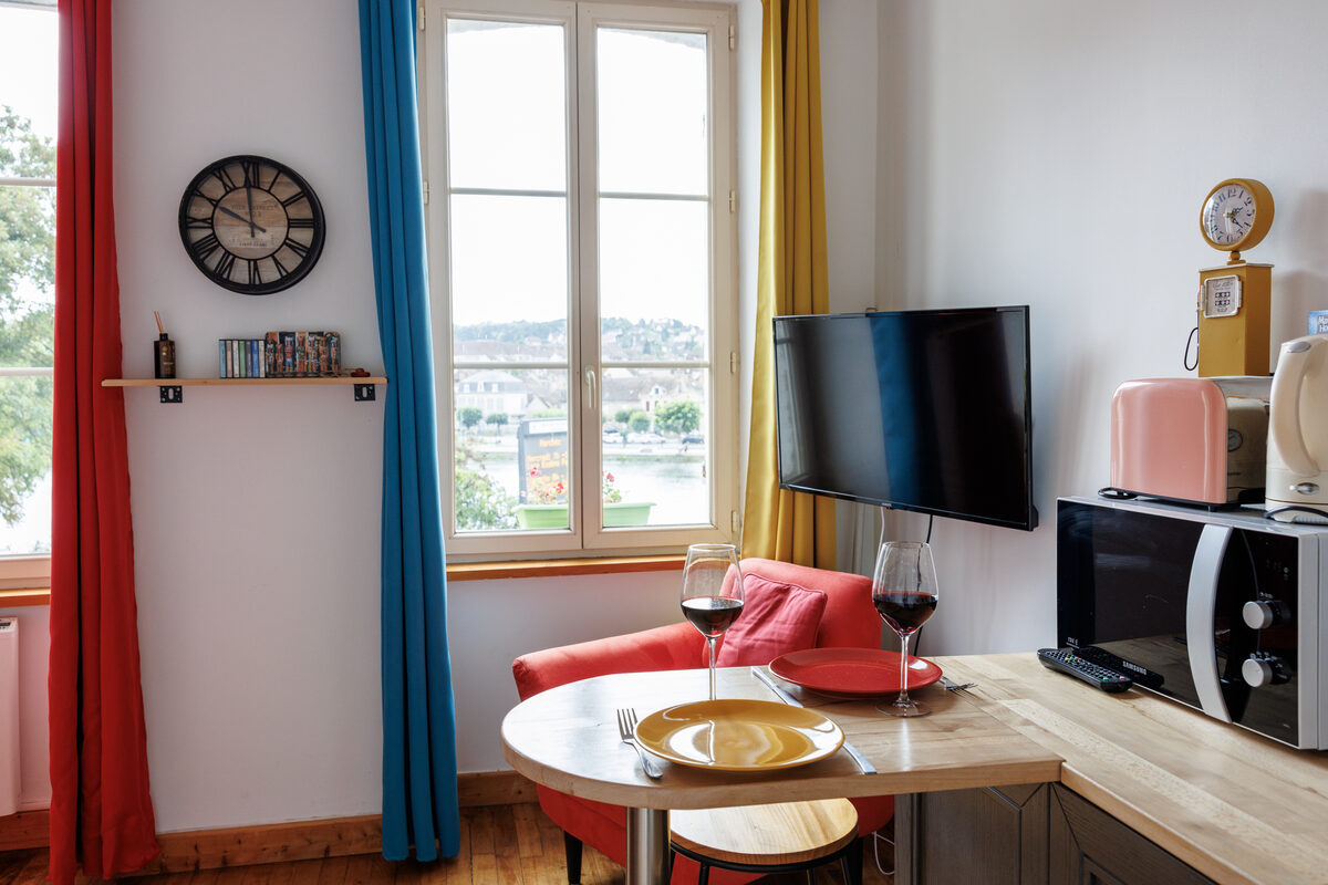Studio Le Cox, salon avec vue sur l'Yonne, table ronde et canapé coloré — KM99 Pont-sur-Yonne