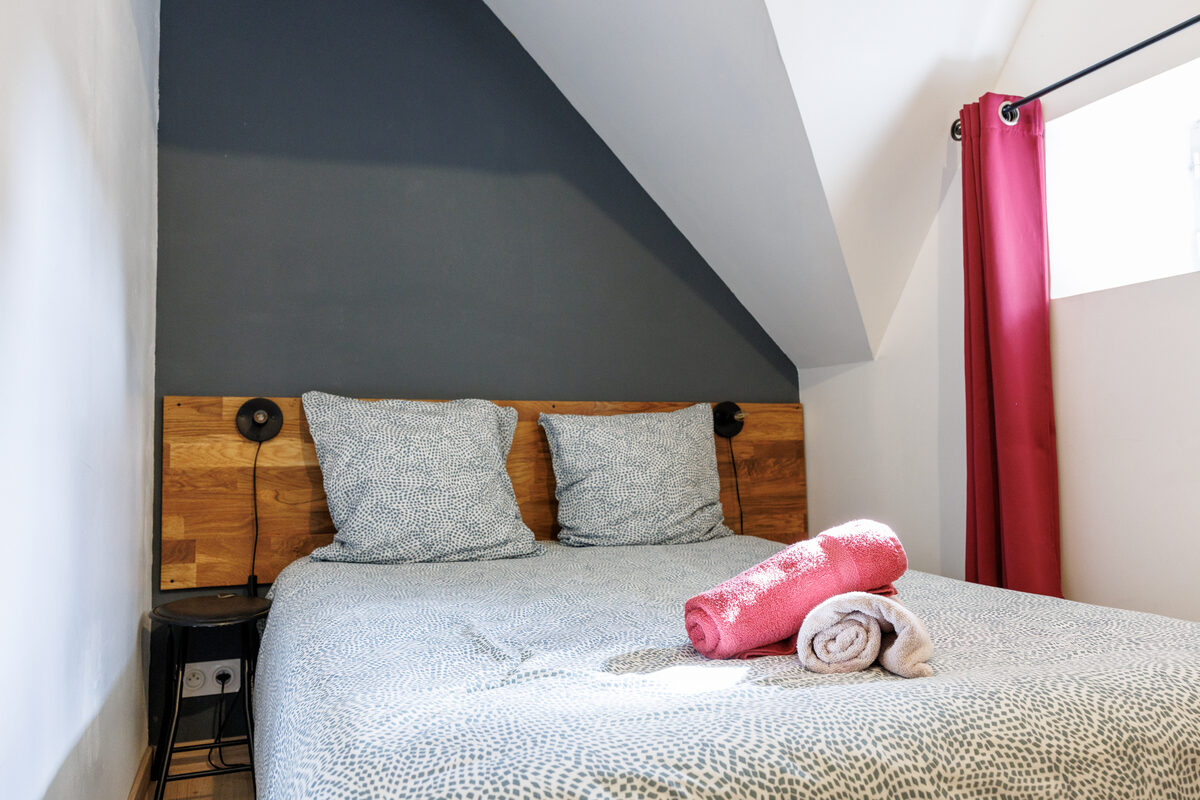 Deuxième chambre L'Indus sous les combles, lit double, tête de lit bois et rideau bordeaux — La Graineterie