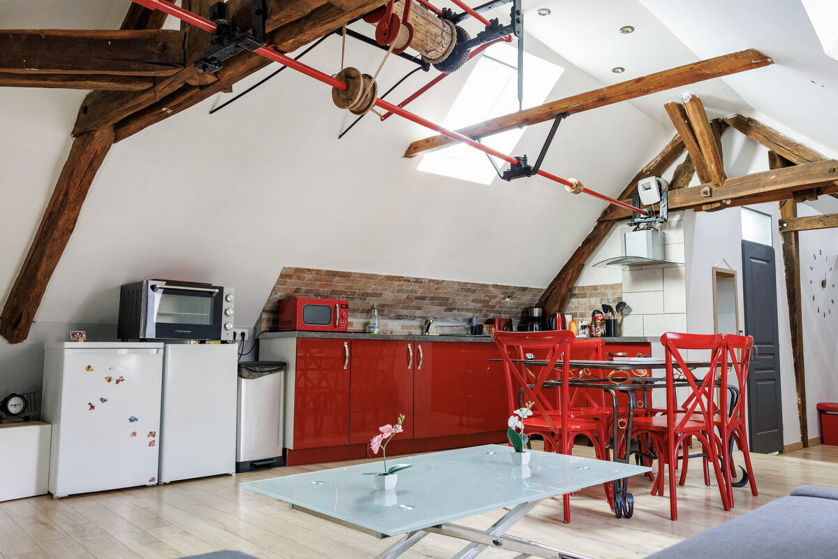Loft L'Indus, grande pièce de vie avec poutres apparentes, cuisine rouge laquée et biplan décoratif — La Graineterie Pont-sur-Yonne