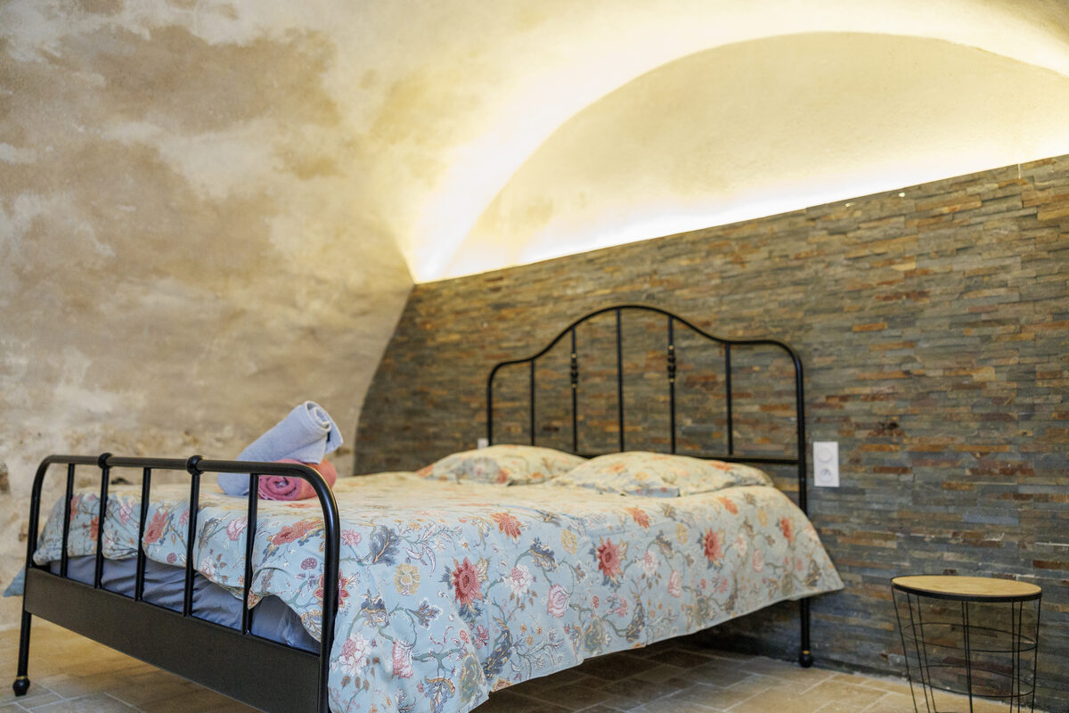 Chambre La Vitrine, lit double fer forgé sous voûte en pierre éclairée, mur ardoise — La Graineterie Pont-sur-Yonne