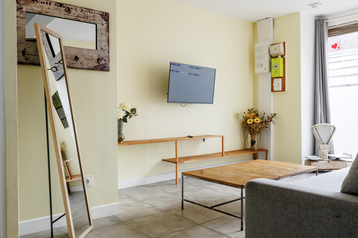 Salon La Vitrine, grands miroirs, TV murale, murs jaune pâle et table basse bois métal — La Graineterie